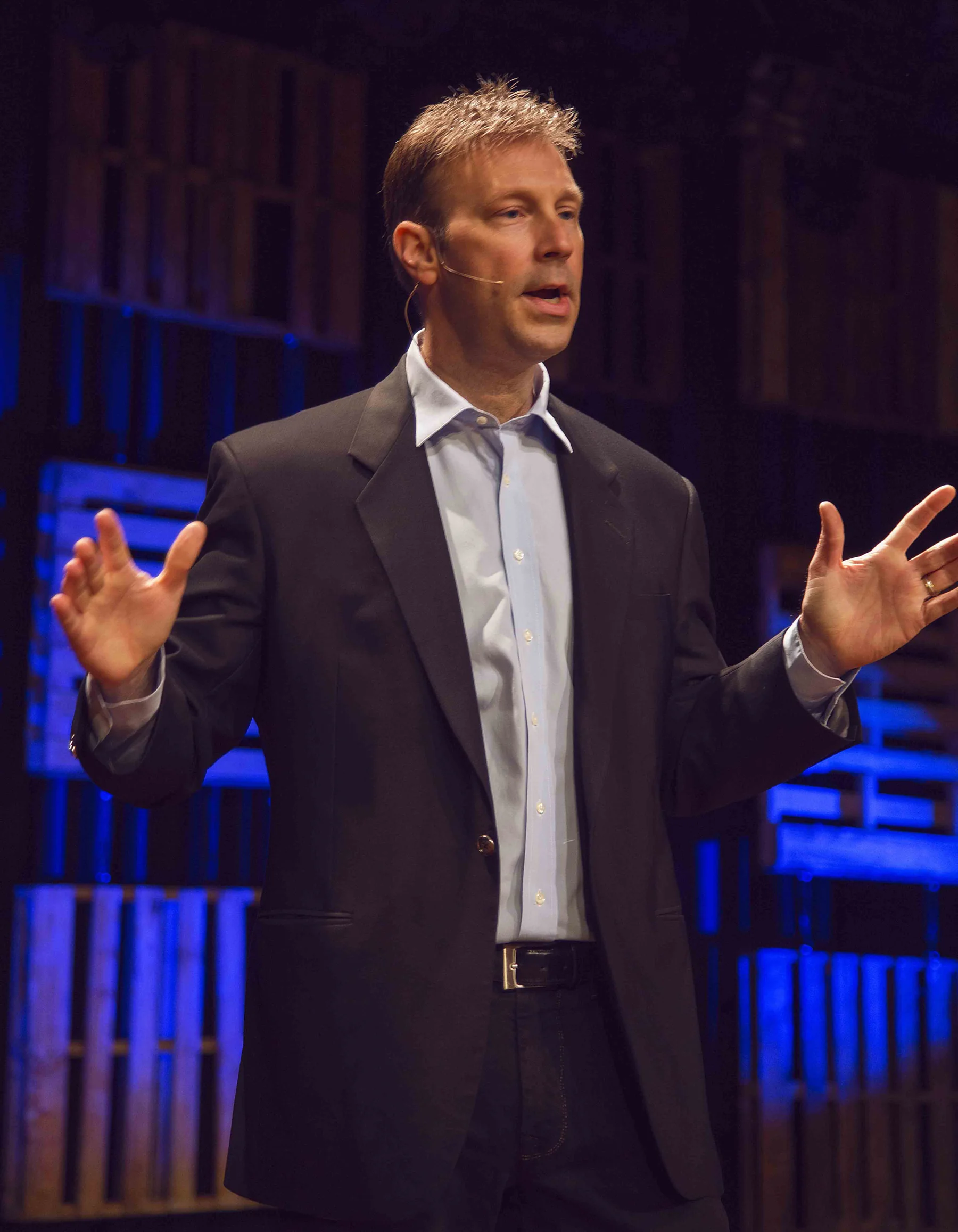 Bruce Eicher speaking onstage with a headset microphone.